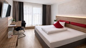 A modern hotel room with a bed, desk, chair, and a TV. - Hotel Asgard (Gersthofen)