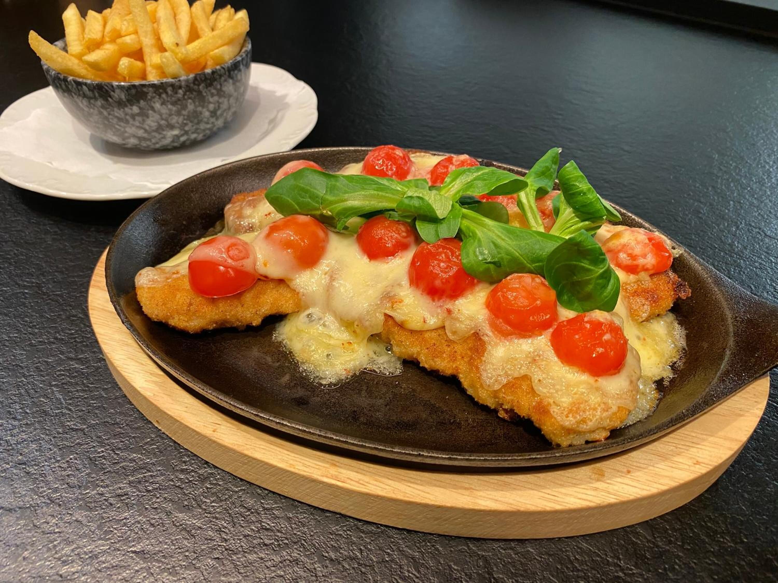 Prato com escalope à milanesa, queijo, tomate cereja e manjericão em um prato escuro.