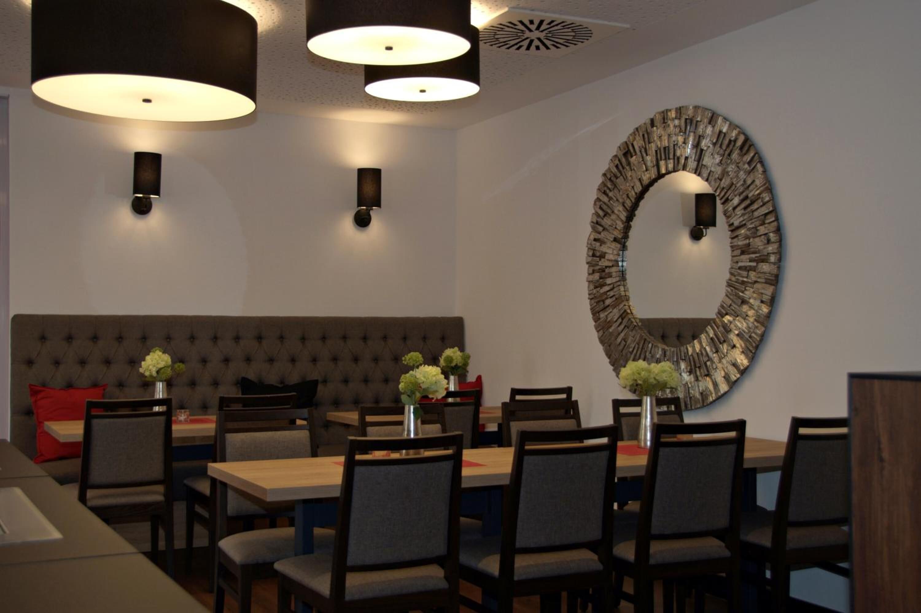 Un espace de salle à manger moderne agrémenté d’un grand miroir rond, de luminaires suspendus et d’une tête de lit capitonnée.