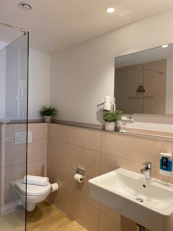 Un baño moderno con cabina de ducha de vidrio, inodoro, lavabo y espejo sobre el lavabo.