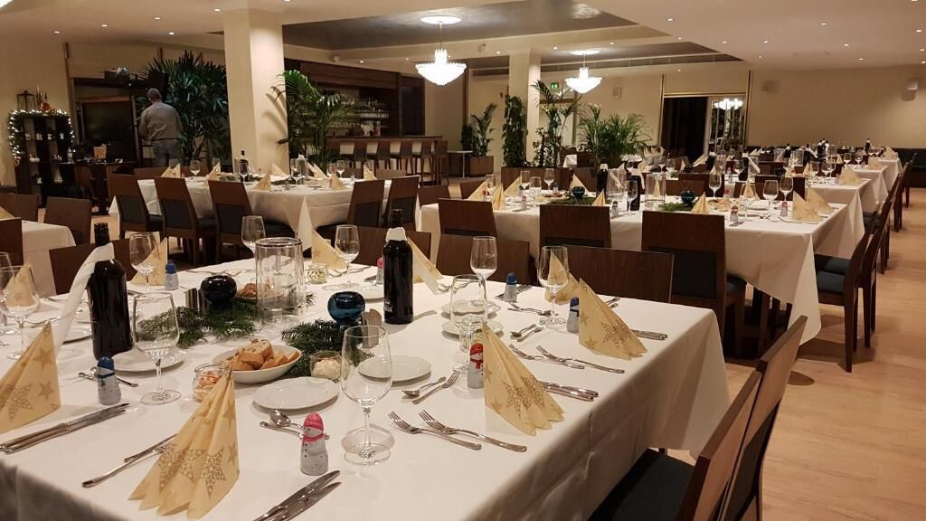 Un salón de banquetes con varias mesas dispuestas para comer, cada una con manteles blancos, cubertería ordenada y cristalería.