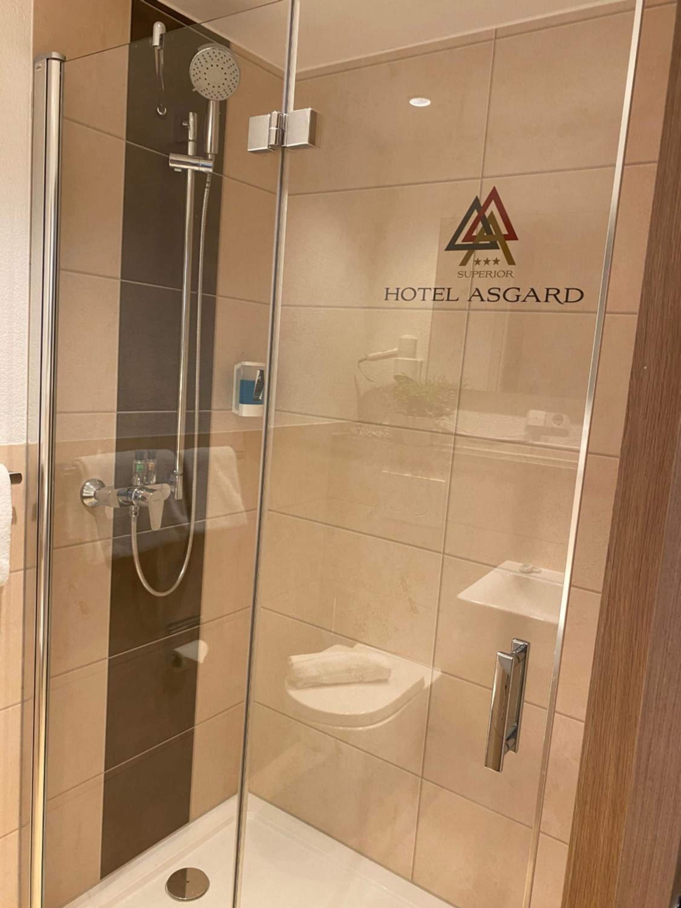 A glass-enclosed shower stall with a handheld showerhead and a wall-mounted faucet.