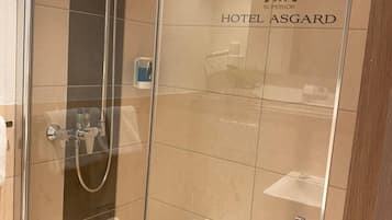 A glass-enclosed shower stall with a handheld showerhead and a wall-mounted faucet.