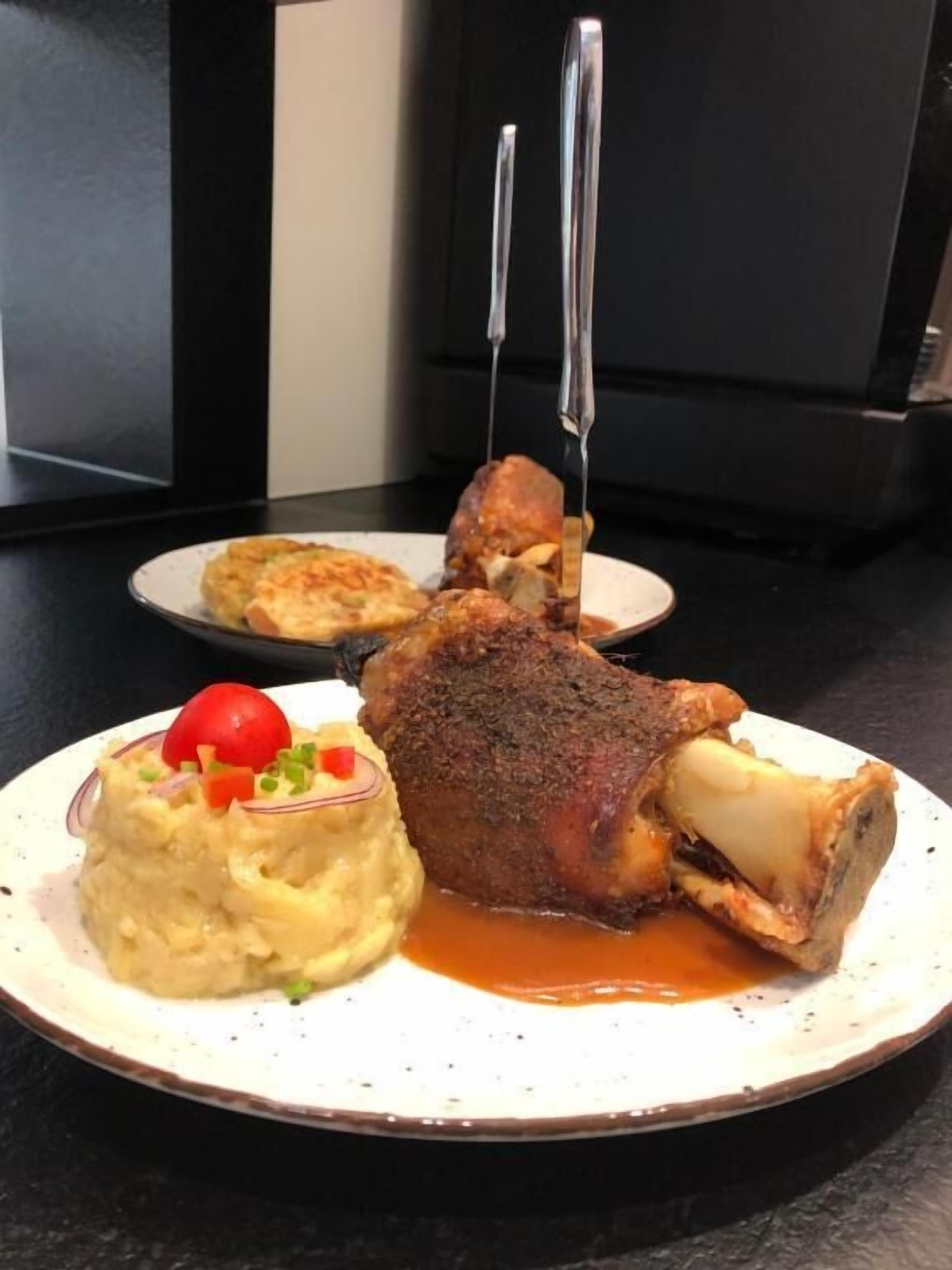 A plate with a roasted meat, mashed potatoes, and a cherry tomato garnish.