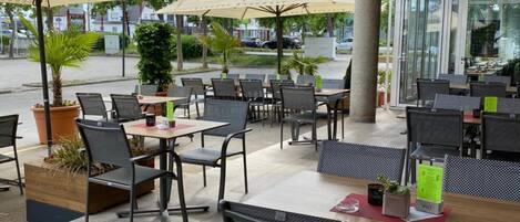 Un café en plein air avec des tables et des chaises, des parasols et des plantes en pot.