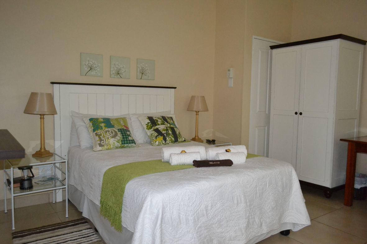 A neatly made bed with a white headboard, two bedside lamps, and decorative pillows. A wardrobe is visible to the right.