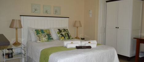 A neatly made bed with a white headboard, two bedside lamps, and decorative pillows. A wardrobe is visible to the right.