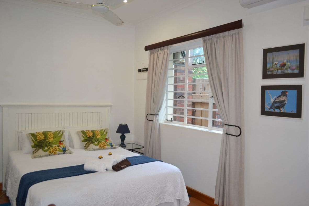 Quarto bem organizado com cama, mesa de cabeceira, luminária e janela com cortinas.