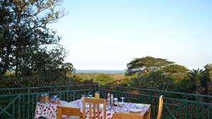 Un espacio para comer al aire libre con una mesa dispuesta para dos, rodeado por una barandilla verde, con vistas a un paisaje pintoresco.