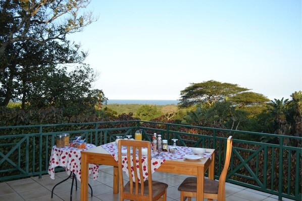 Un espacio para comer al aire libre con una mesa dispuesta para dos, rodeado por una barandilla verde, con vistas a un paisaje pintoresco.
