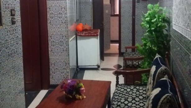 Un pasillo estrecho con paredes estampadas, una puerta de madera, una mesita con un florero, un sofá con diseño y una planta.
