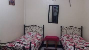 A room with two single beds, a small bench, a mirror, and a wall-mounted air conditioner.