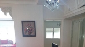 Un comedor con una mesa cubierta con mantel floral, dos sillas, una araña y un cuadro en la pared.