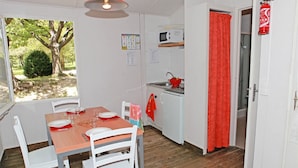 A compact kitchen with white cabinets, a microwave, and a red curtain. - Camping Domaine du Petit Lac (Moustiers-Sainte-Marie)