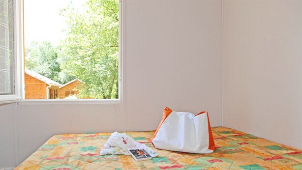 A room with a bed, a window, and a bag on the bed. - Camping Domaine du Petit Lac (Moustiers-Sainte-Marie)