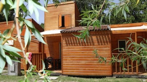 A wooden cabin with a patio, a small window, and a door. - Camping Domaine du Petit Lac (Moustiers-Sainte-Marie)