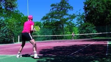 A tennis court with a net, surrounded by trees and a clear sky.