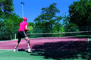 Un court de tennis avec un filet, entouré d’arbres et sous un ciel dégagé.