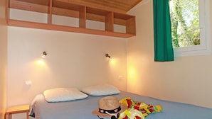 A bedroom with a bed, pillows, a hat, and a blanket. - Camping Domaine du Petit Lac (Moustiers-Sainte-Marie)