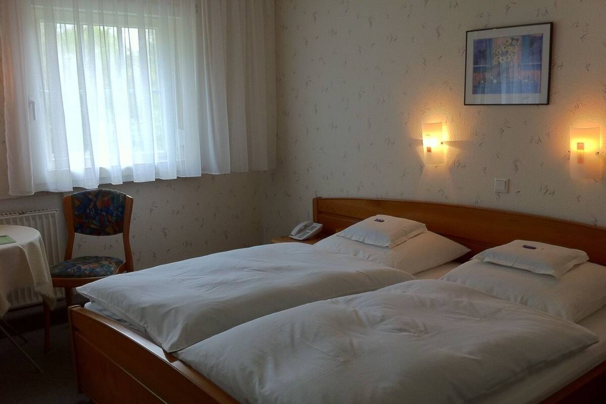 Habitación de hotel con dos camas individuales, una silla, una mesa y un radiador.