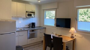 A compact kitchen with a microwave, stove, and sink. There's a dining table with chairs and a TV mounted above it. - Hotel Wintersmühle (Bielefeld)