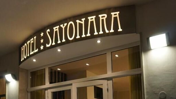 A hotel entrance with a glass door, a sign above the door, and a potted plant to the right. - Hotel Sayonara (Cervia)