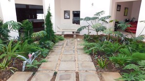 A courtyard with a stone pathway, various plants, a bench, and framed pictures on the walls. - 02 Phoka Trading (Pretoria)