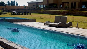 A swimming pool with a netted safety barrier, lounge chairs, and a patio area with tables and chairs. - 02 Phoka Trading (Pretoria)