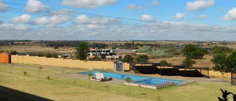 A residential area with a swimming pool, a wooden deck, and a view of distant buildings and fields.