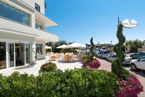 A hotel with outdoor seating, a clear sky, and a parking area. - Hotel Oriente (Cervia)