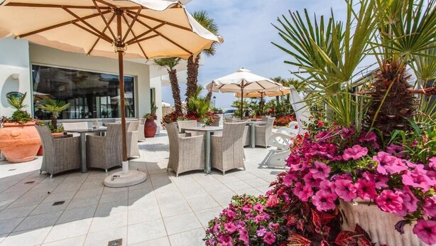 An outdoor patio area with tables and chairs, umbrellas, and potted plants. - Hotel Oriente (Cervia)