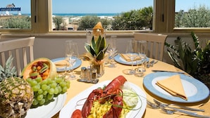 A table set with a lobster, pineapple, grapes, and a salad, overlooking a scenic view. - Hotel Oriente (Cervia)