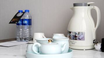 A tea set with a teapot and cups on a tray, a water bottle, and a coffee maker on a table.