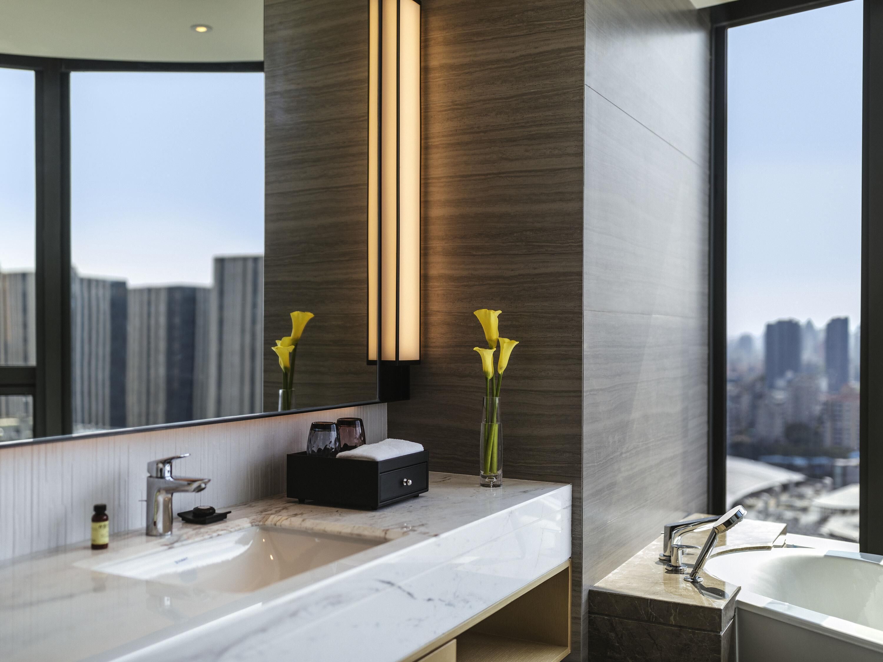 A modern bathroom with a large mirror, a sink, a bathtub, and a vase with flowers.