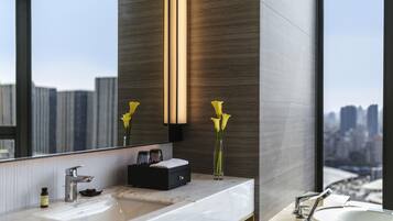 A modern bathroom with a large mirror, a sink, a bathtub, and a vase with flowers.