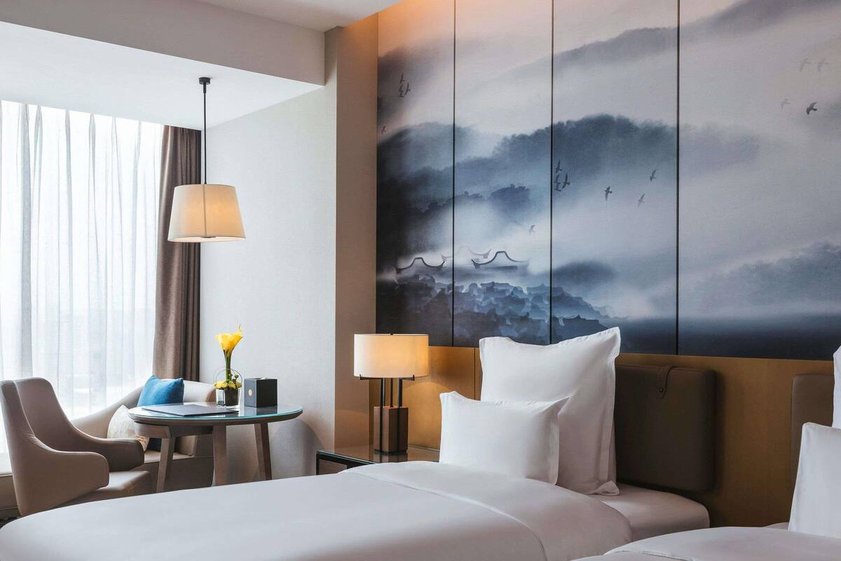 Ein Hotelzimmer mit zwei Betten, einem Schreibtisch mit Lampe, einem Stuhl und einem großen Wandbild.