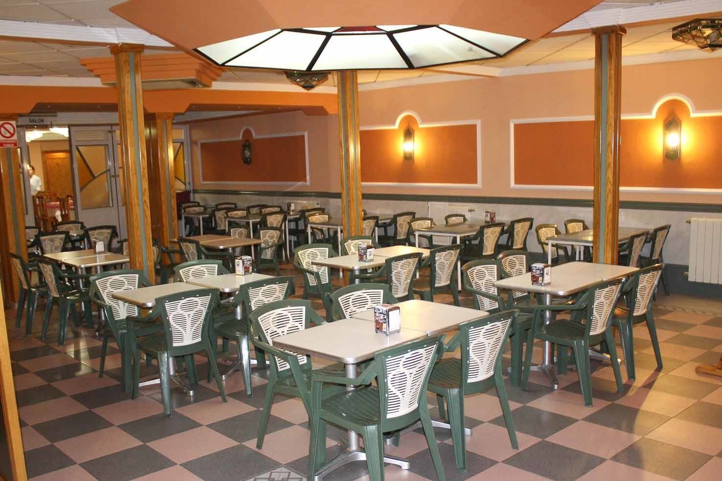 Een restaurant met meerdere tafels en stoelen, een zwart-wit geruit vloertje en een plafondventilator.