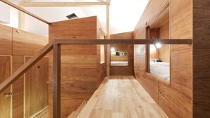 Interior de madera con una escalera central, paredes de madera y una cama al fondo.