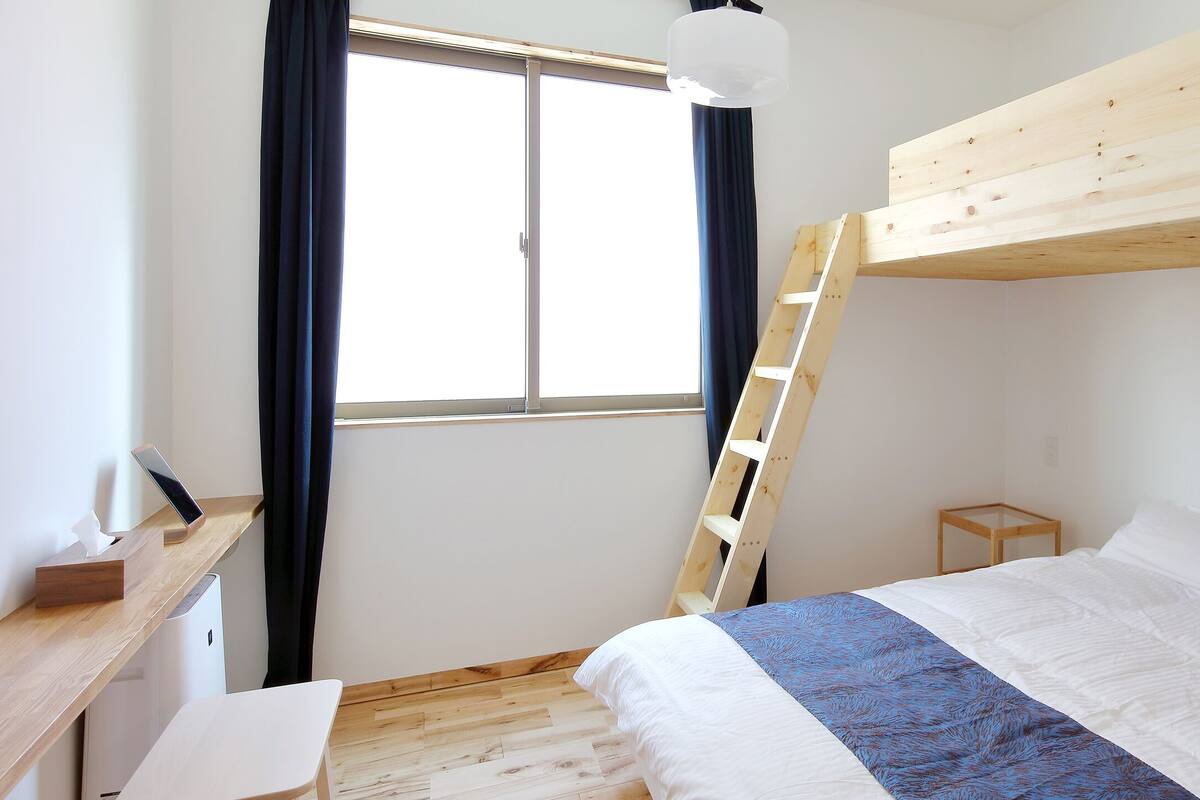 A bedroom with a bunk bed, a desk with a computer, and a window with curtains.