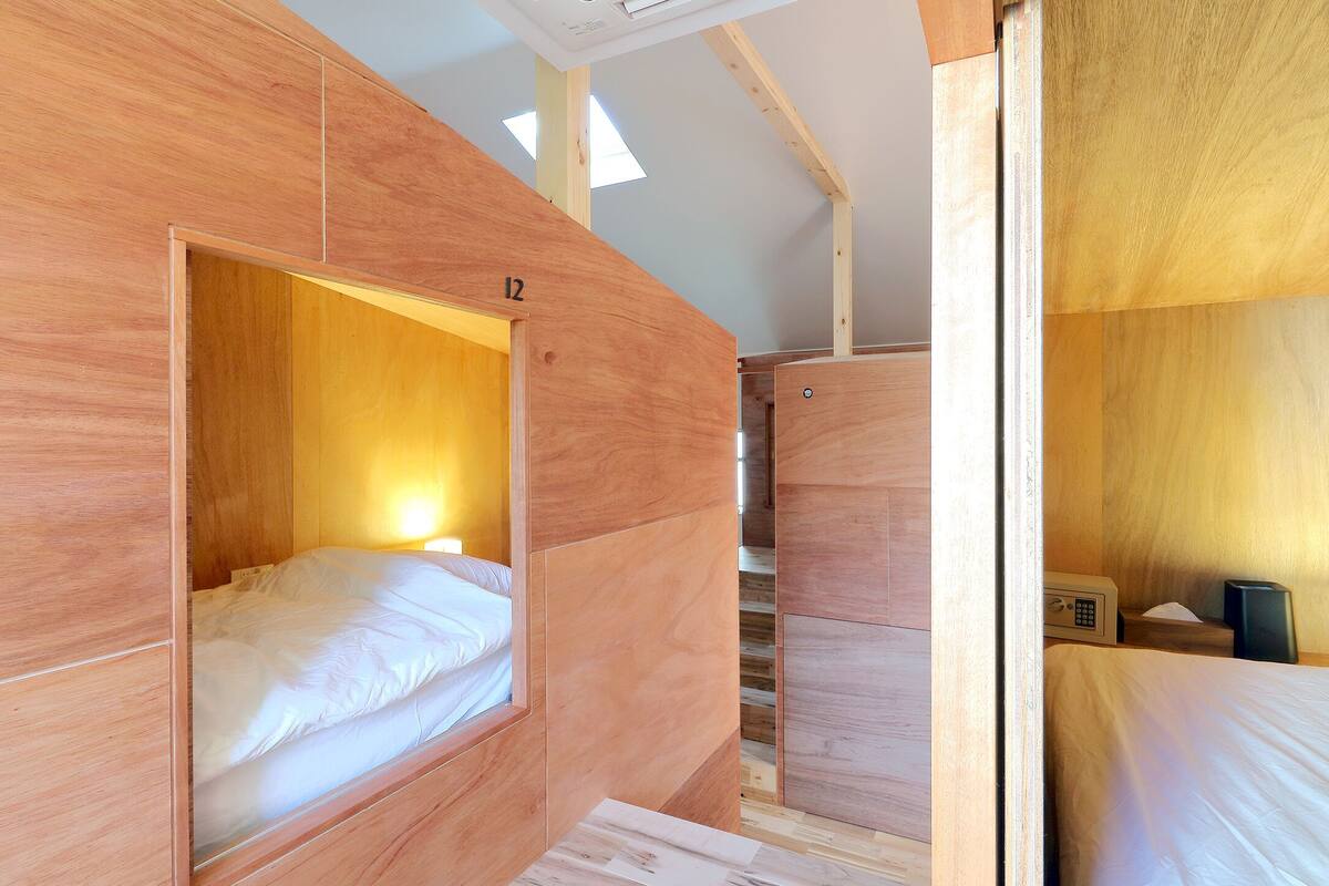A modern hotel room with a wooden interior, a bed, a desk, and a small seating area.
