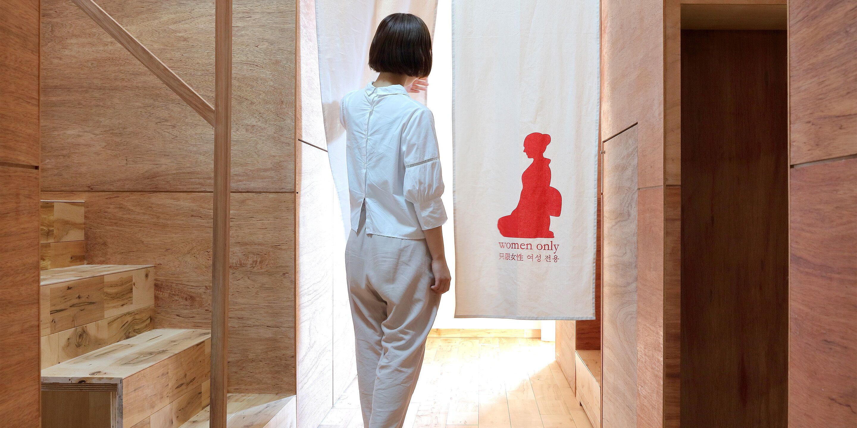 A person walking through a wooden interior space with a sign reading "women only" and a silhouette of a woman.