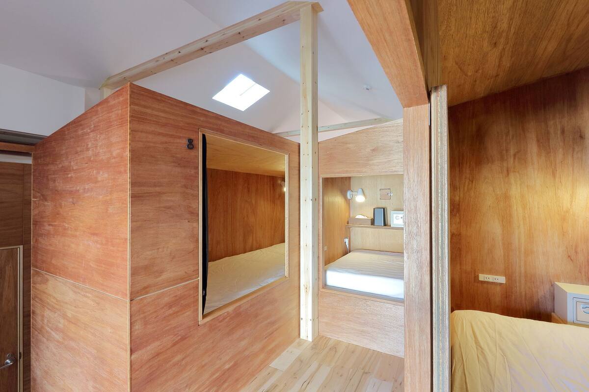 A room with wooden walls, a bed, a bedside table, a mirror, and a ceiling light.