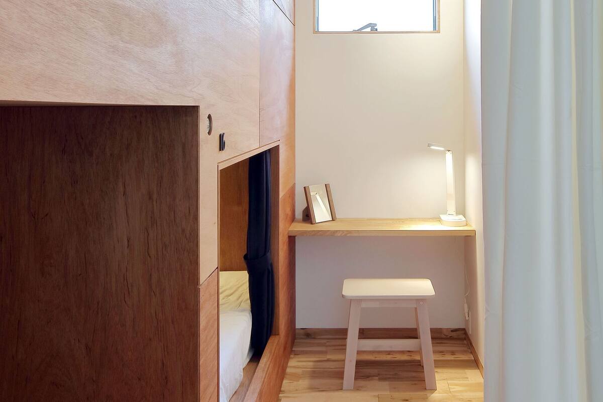 A compact room with a wooden wardrobe, a desk with a chair, and a small window.