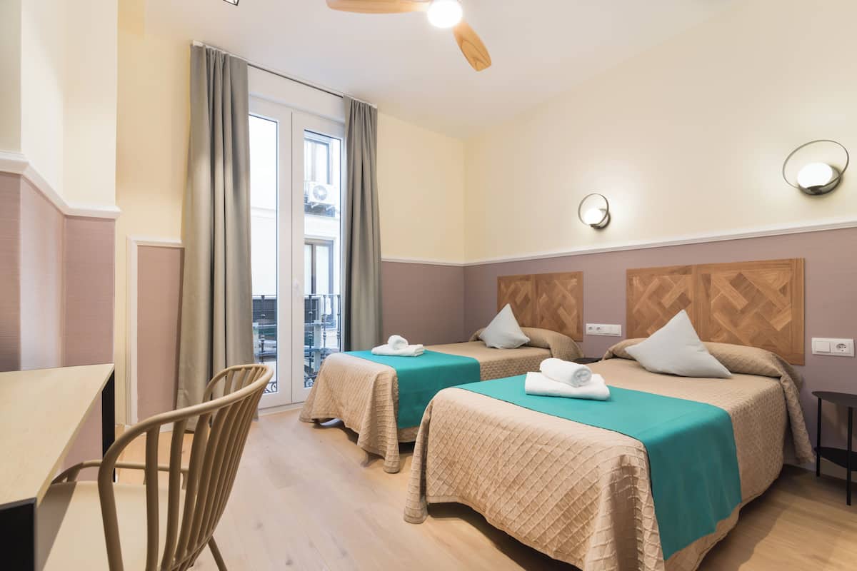 Quarto de hotel com duas camas, uma mesa e uma cadeira.