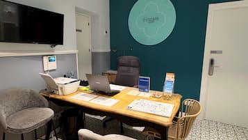 Een vergaderruimte met een houten tafel, stoelen, een televisie en een scherm aan de muur.