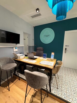 A conference room with a wooden table, chairs, a television, and a wall-mounted screen. - Hostal Evocare Madrid (Madrid)