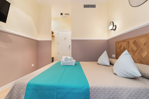 A hotel room with a bed, a bathroom door, a towel rack, and a wall-mounted light fixture. - Hostal Evocare Madrid (Madrid)