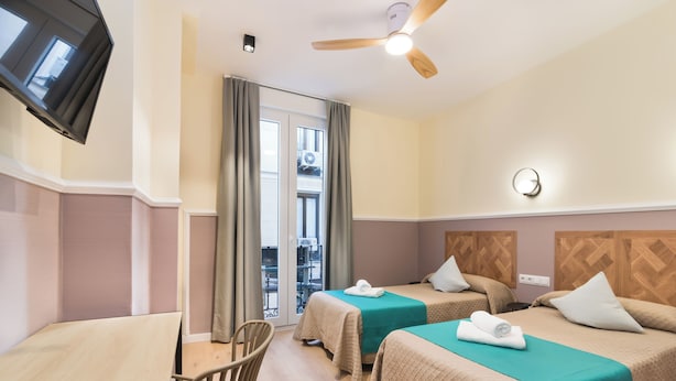 Habitación de hotel con dos camas, televisión, ventilador de techo y vistas al balcón exterior.
