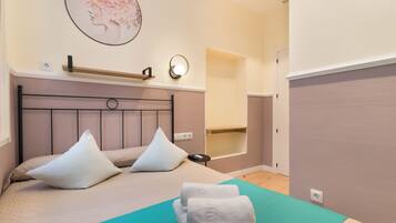 A neatly arranged bedroom with a bed, pillows, a bedside table, a wall-mounted shelf, and a wall-mounted light fixture.