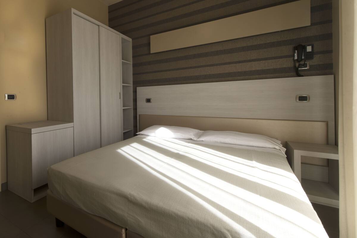 A bedroom with a bed, a wardrobe, and a headboard with built-in lighting.